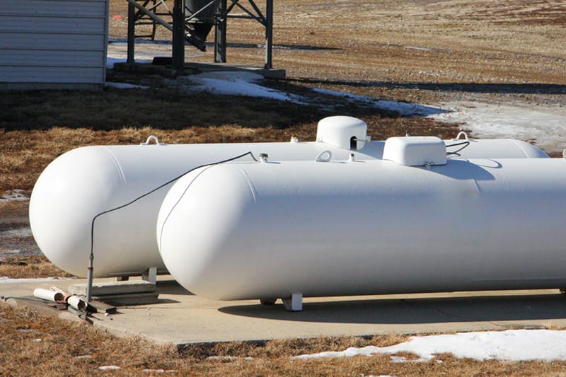 Two white propane tanks sitting outside on top of a piece of concrete