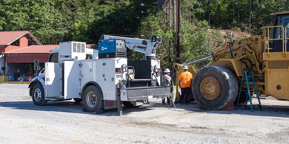 White Stellar mechanic service truck with open compartment doors and mounted crane assisting jobsite maintenance on a large wheel loader.
