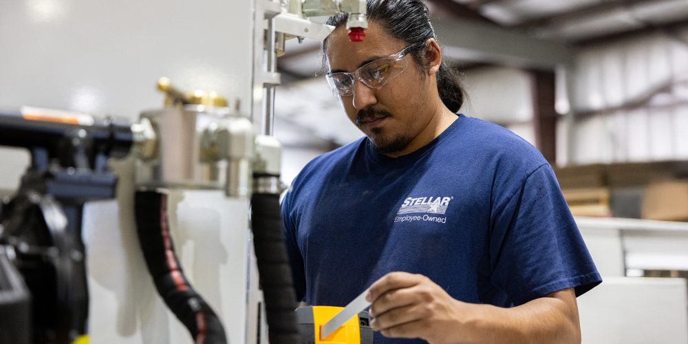 A Stellar employee wearing a "100% Employee-Owned" t-shirt, focused on assembling a Stellar product on the manufacturing floor.