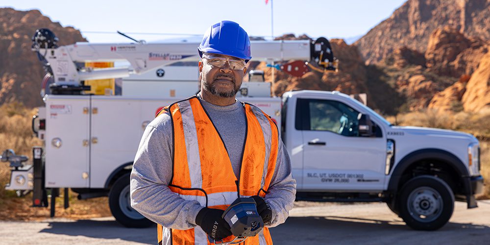 Technician in front of a TMAX mechanic truck near rocky terrain.