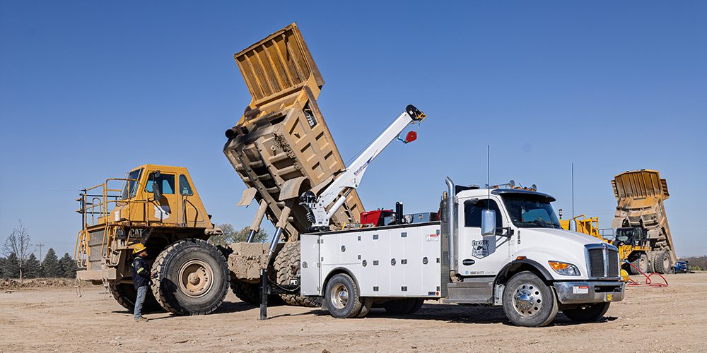 Mechanic truck with crane in front of a large dump truck.