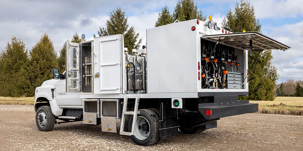 White Stellar single-axle lube truck with open service compartments showing oil tanks, hose reels, and tool storage, parked in an outdoor field.