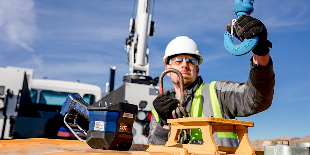 Wheeler Cat service technician guiding a crane hook with a Stellar® CDTpro™ wireless remote control in the foreground.
