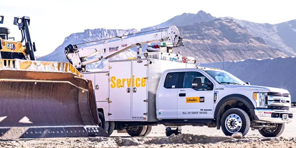 Wheeler Cat mechanic truck equipped with a Stellar® 7630 service crane parked alongside a Cat bulldozer at a jobsite.