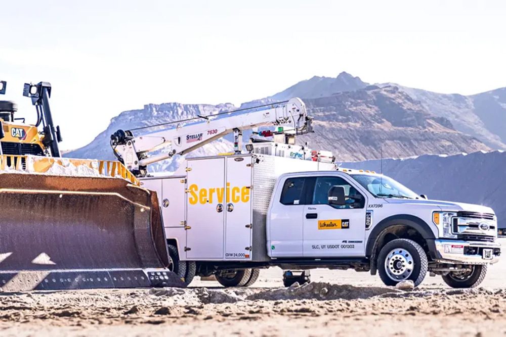 Wheeler Cat mechanic truck equipped with a Stellar® 7630 service crane parked alongside a Cat bulldozer at a jobsite.