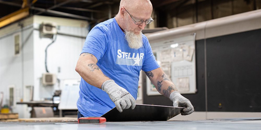 Stellar fabrication employee with blue shirt holding piece of steel in hands.