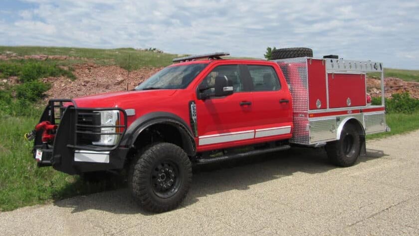 Red Midwest Fire brush truck on road in park setting.