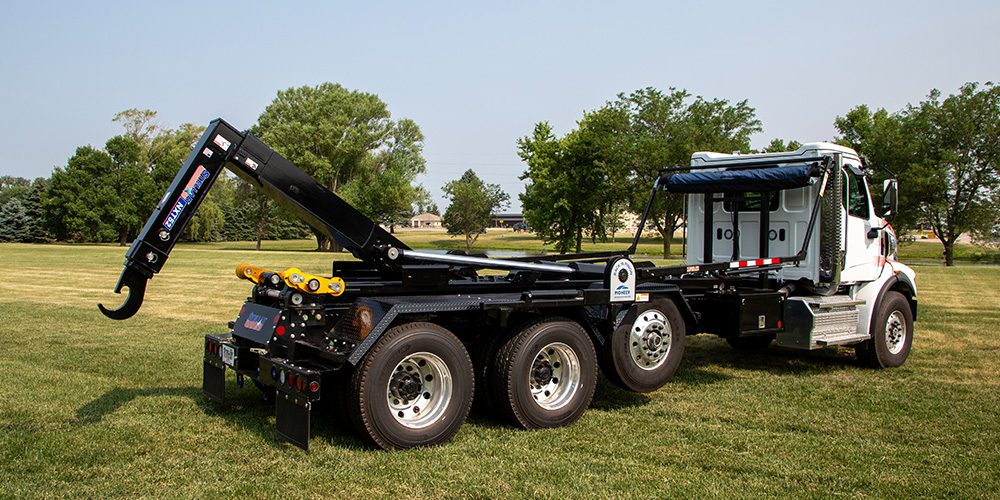 A white work truck equipped with a black Stellar NXT52 Hydraulic Hooklift parked on grass.