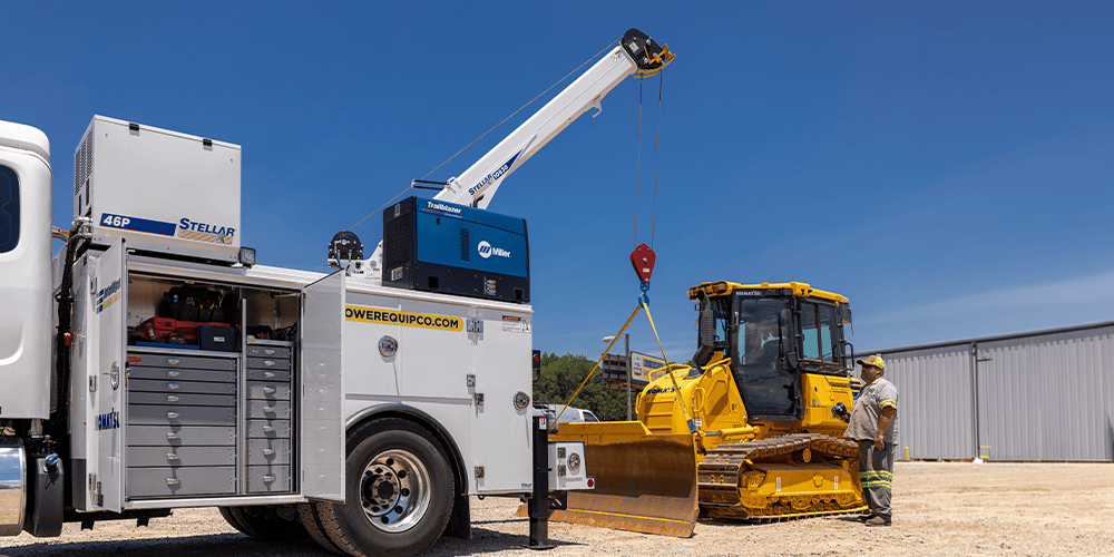 Stellar mechanic truck with open drawer tool storage and extended telescoping crane positioned next to a yellow crawler tractor.