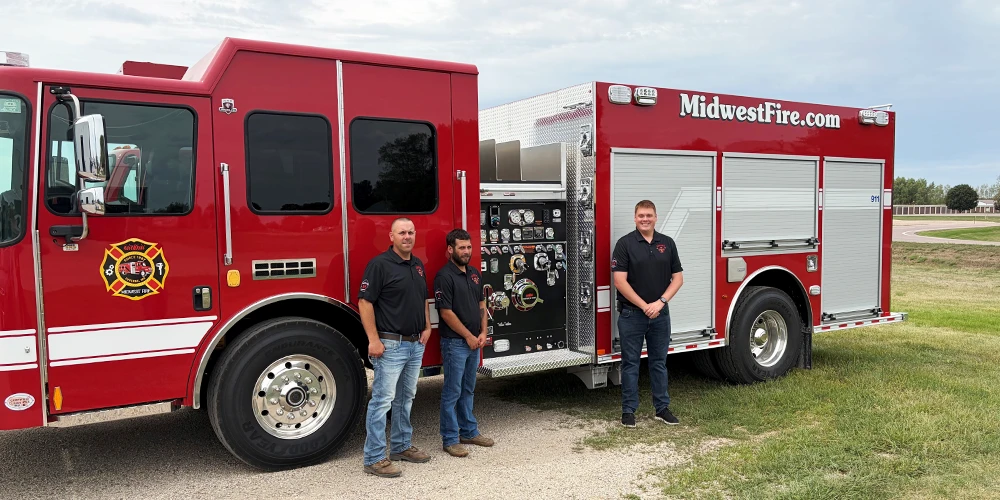 Three Stellar employee-owners who serve as Garner volunteer firefighters stand beside a red Midwest Fire truck.